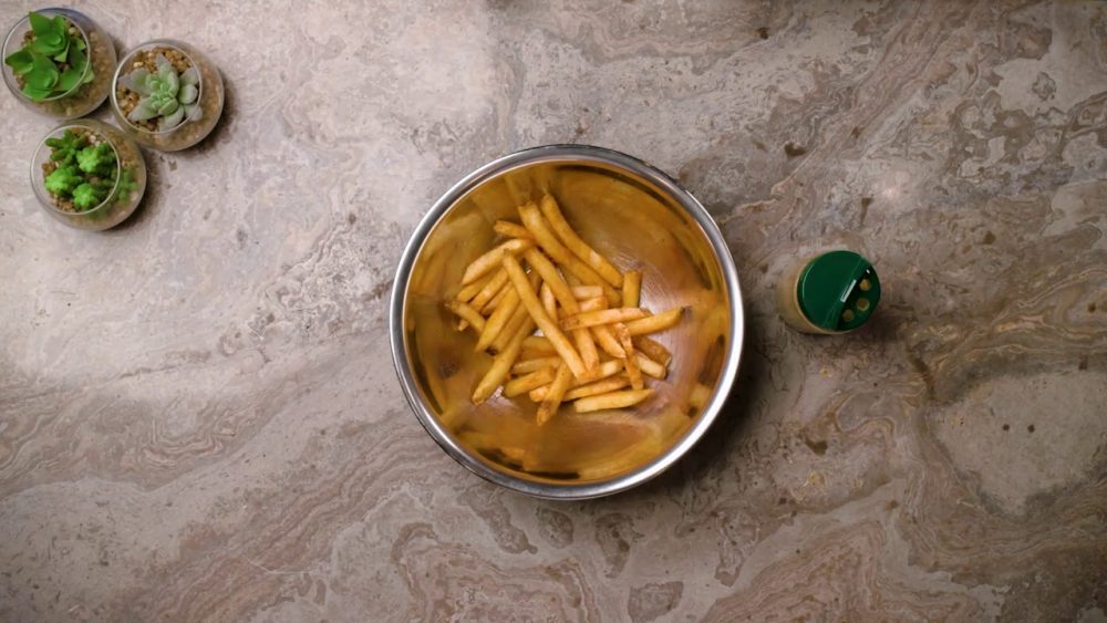 A silver bowl filled with French fries next to three small succulents in glass pots.