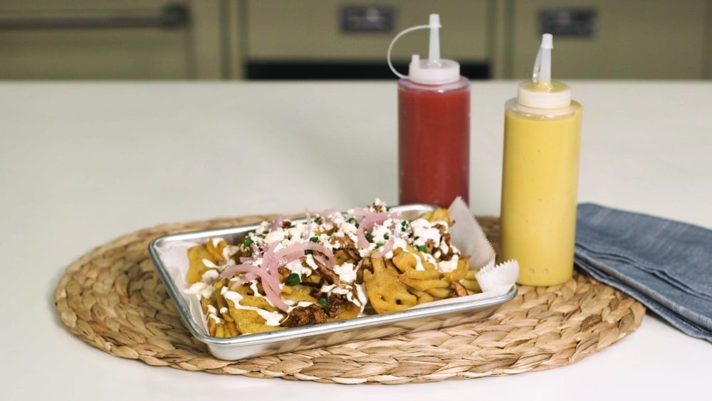 French fries topped with brisket, onions, and more sitting on a silver serving tray.