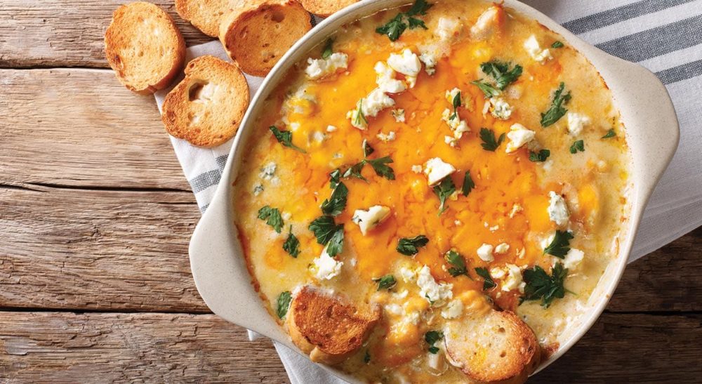 Buffalo cheddar dip topped with Blue cheese crumbles in a white ceramic pan.