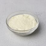 A clear glass bowl filled with powdered dairy flavor used by food manufacturers in their food products.