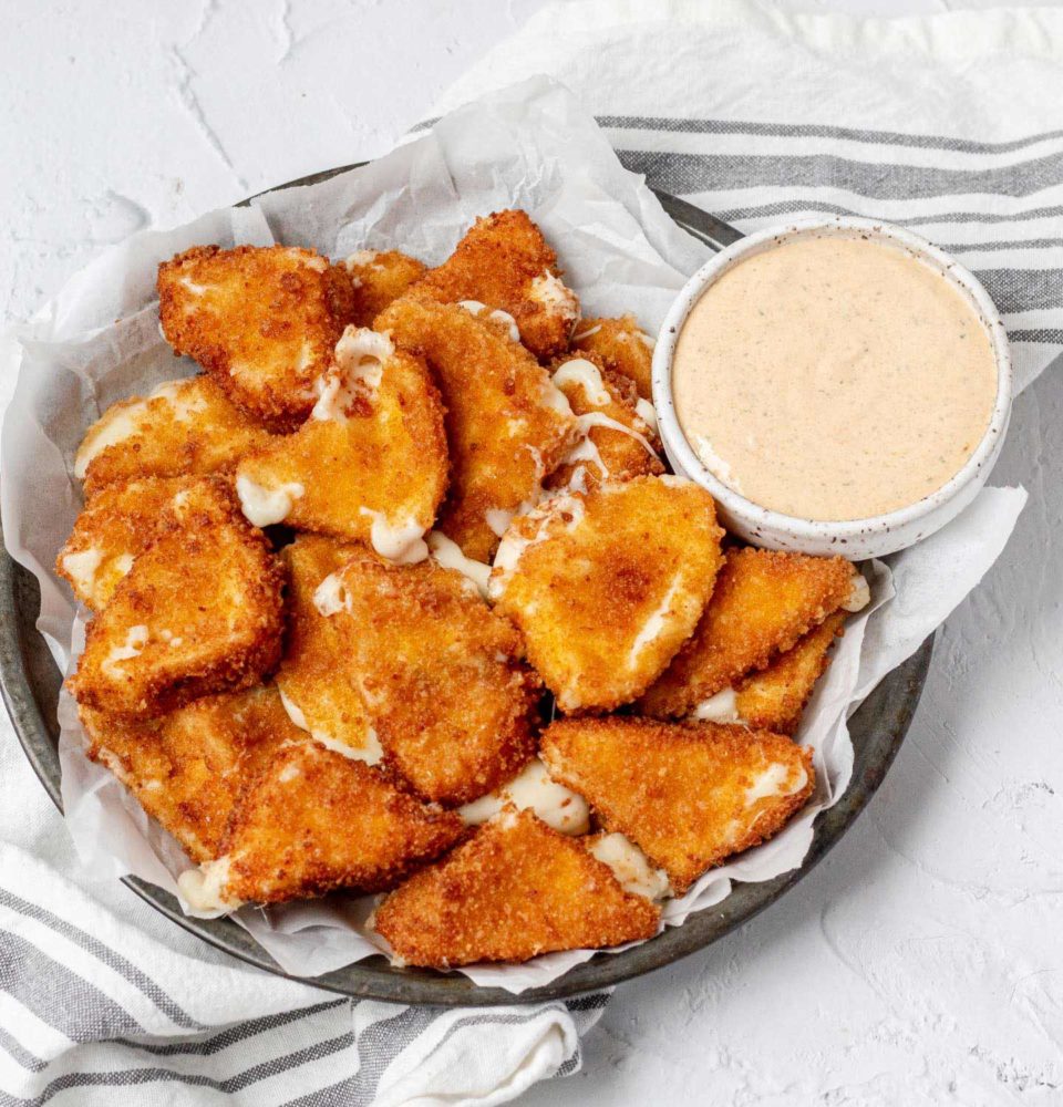 A large bowl filled with breaded and fried cheese next to a bowl filled with a creamy dip.