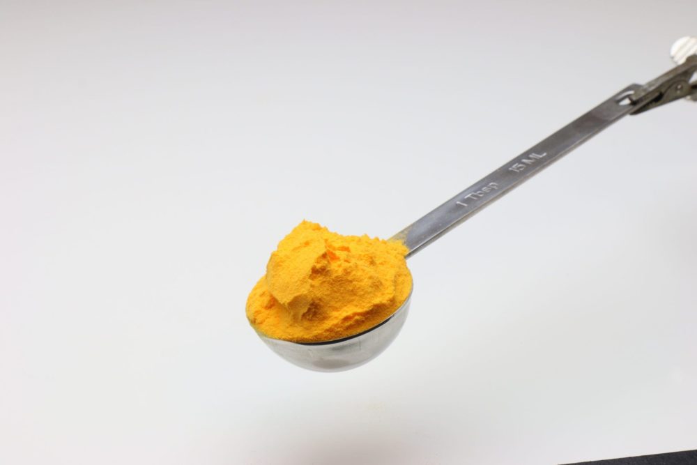 A silver tablespoon measuring cup full of cheese seasoning powder.